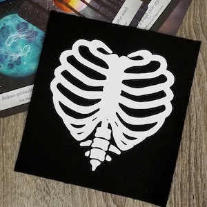 May include: White ribcage design on a black fabric patch. The ribcage is shaped like a heart.