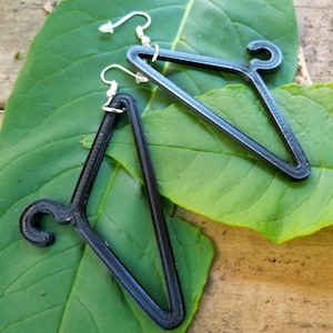 May include: A pair of black triangle-shaped earrings with a hanger hook design. The earrings are made of a textured material and have silver hooks.