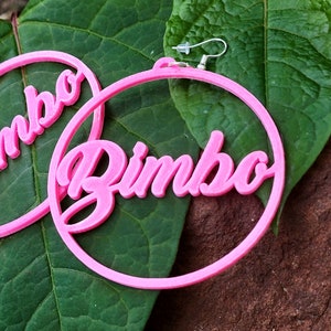May include: Pink hoop earrings with the word "Bimbo" written in a bold, cursive font.