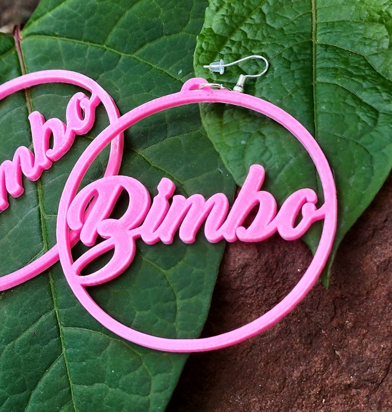 May include: Pink hoop earrings with the word "Bimbo" written in a bold, cursive font.