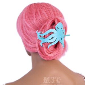 May include: A light blue octopus hair clip with a textured surface. The clip is in the hair of a person with pink hair.