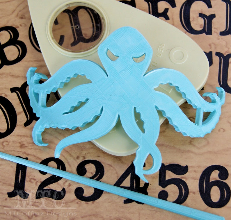 May include: A light blue octopus cutout with a menacing expression. The octopus is placed on a wooden surface with black numbers and letters.