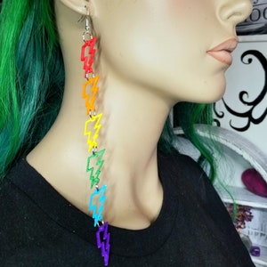 May include: Rainbow colored lightning bolt dangle earrings. Each earring features a chain of lightning bolts in red, orange, yellow, green, blue, indigo, and violet.