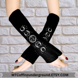 May include: A pair of black fingerless arm warmers with a white moon and stars design. The arm warmers are made of a soft, stretchy fabric and are perfect for keeping your arms warm in the cooler months.
