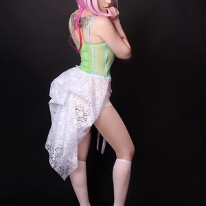 Pu&ograve; includere: Una donna indossa una gonna di pizzo bianco con un corpetto a righe verdi e bianche, una parrucca rosa e tacchi bianchi.