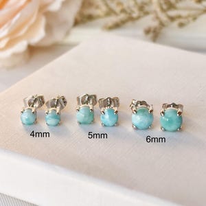 May include: A collection of silver stud earrings with light blue, oval-shaped gemstones. The earrings are displayed in pairs, with sizes of 4mm, 5mm, and 6mm. The gemstones have a smooth, polished appearance.