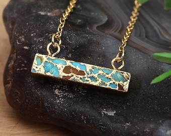 May include: Gold chain necklace with a turquoise and gold bar pendant. The pendant has a textured surface and a hammered finish.