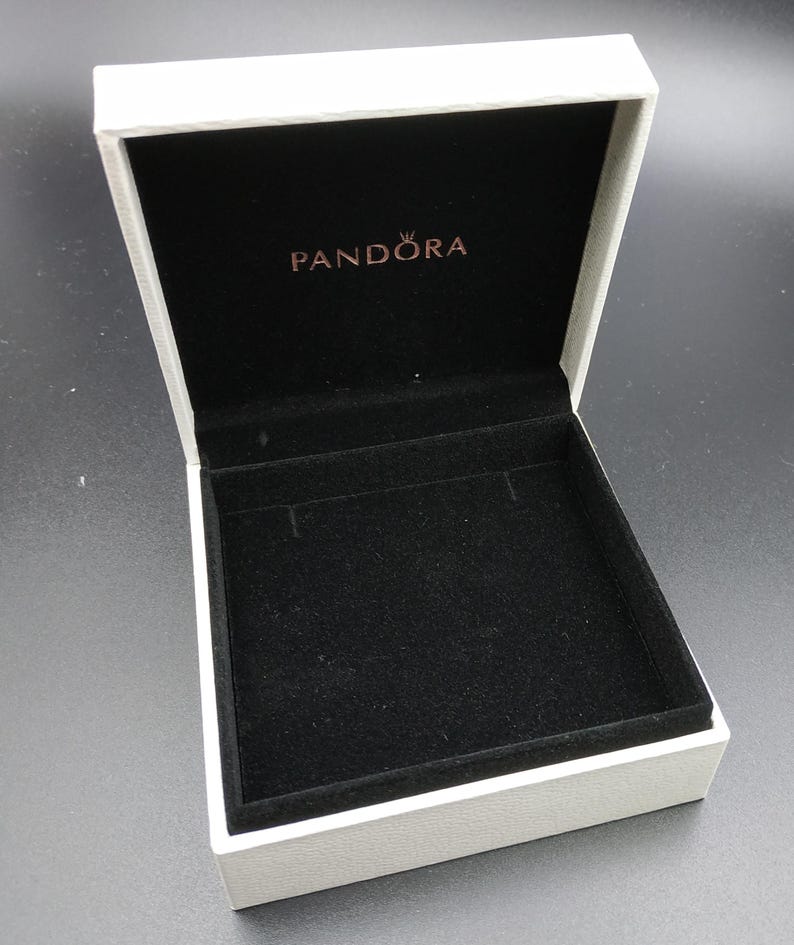 May include: White jewelry box with a black velvet interior. The box has the word "PANDORA" printed on the lid in gold lettering.