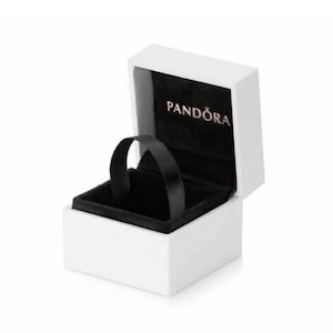 May include: White jewelry box with a black velvet interior and a black ribbon. The box has the word "PANDORA" printed on the lid.