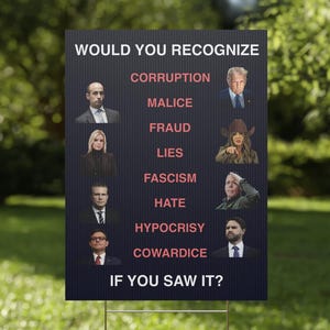 May include: A dark blue yard sign with the text "WOULD YOU RECOGNIZE" and a list of words like "CORRUPTION" and "MALICE." The sign also features images of various people. The sign is placed in a grassy garden.