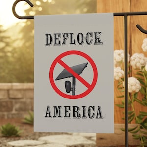 May include: A rectangular garden flag featuring a light grey background with the text DEFLOCK AMERICA in black block letters. In the centre, a red circle with a diagonal line overlays a graphic of a black solar-powered security camera.