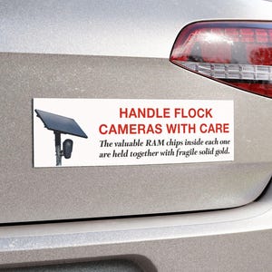 May include: A rectangular bumper sticker on a silver car featuring a graphic of a solar-powered security camera and the text: HANDLE FLOCK CAMERAS WITH CARE. The valuable RAM chips inside each one are held together with fragile solid gold.