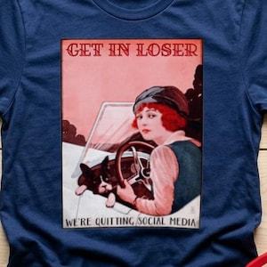 May include: Navy blue t-shirt with a vintage-style graphic that reads "GET IN LOSER" above an illustration of a woman in a car with a dog. The text "WE'RE QUITTING SOCIAL MEDIA" is below the image. A pair of blue jeans and a red spatula are also in the image.