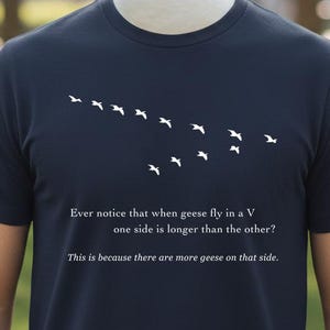 May include: Navy blue t-shirt with a white graphic of geese in a V formation. The text reads, "Ever notice that when geese fly in a V one side is longer than the other? This is because there are more geese on that side."
