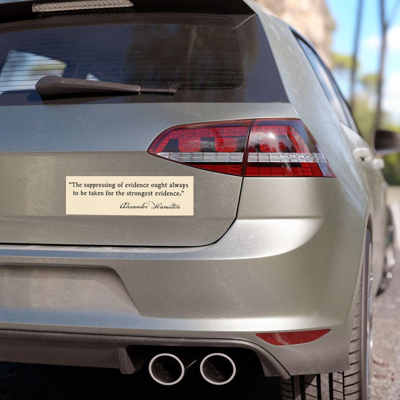 May include: A rectangular bumper sticker with a quote by Alexander Hamilton, in black text on a cream background, is affixed to the rear of a silver car. The quote reads, "The suppressing of evidence ought always to be taken for the strongest evidence."
