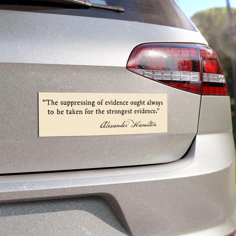 May include: A rectangular bumper sticker with a cream background is affixed to the back of a silver car. The sticker features a quote by Alexander Hamilton in black text: "The suppressing of evidence ought always to be taken for the strongest evidence."