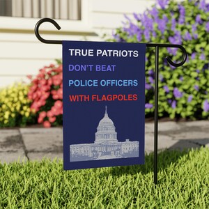 May include: A blue garden flag with white text that reads "True Patriots Don't Beat Police Officers With Flagpoles". The flag also features a white silhouette of the US Capitol building.