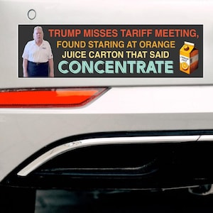 May include: A black and orange bumper sticker with a white border. The sticker features a photo of a man in a white shirt and a black tie. The text on the sticker reads 