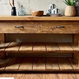 May include: A rustic wooden kitchen island with two drawers and two shelves. The island is made of reclaimed wood and has a natural finish. It features black metal drawer pulls.