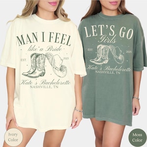 May include: Ivory and moss-colored t-shirts with text and graphics. The ivory shirt says "MAN I FEEL like a Bride" with a cowboy boot and hat graphic. The moss shirt says "LET'S GO Girls" with a similar graphic. Both shirts say "Kate's Bachelorette, Nashville, TN".