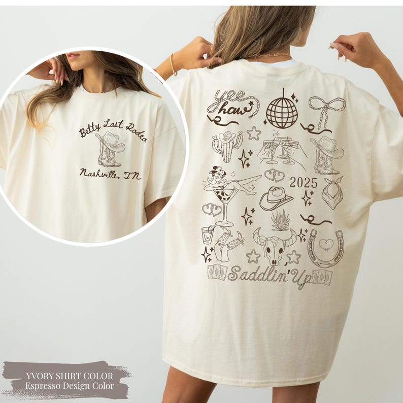 May include: Cream-coloured t-shirt with a black graphic design. The front displays text and a cowboy boot and hat. The back features cowboy-themed illustrations, text, and the year 2025. The shirt has a loose, relaxed fit.