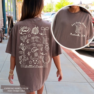 May include: Espresso-coloured t-shirt with ivory graphic designs. The back features cowboy-themed illustrations, the text "Yee Haw", and the year "2025". A smaller design on the upper right says "Some Cowboy Forever, Nashville, TN".