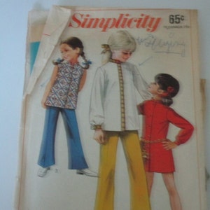 May include: Simplicity sewing pattern 65c for girls' clothing. The pattern shows three girls wearing different outfits. One girl is wearing a white blouse with a gold trim, yellow pants, and a red headband. Another girl is wearing a red dress with a gold chain belt. The third girl is wearing a sleeveless floral top and blue pants.