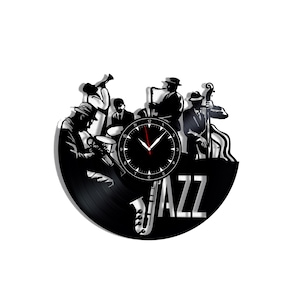 Pode incluir: Um relógio de parede circular feito de um disco de vinil preto com a silhueta de uma banda de jazz com músicos tocando trompete, saxofone e contrabaixo. A palavra JAZZ está recortada em letras prateadas grandes no canto inferior.