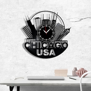 Könnte beinhalten: Schwarze Wanduhr mit einer Silhouette der Skyline von Chicago. Das Zifferblatt ist schwarz mit weißen Ziffern und roten Zeigern. Die Worte "CHICAGO USA" sind darunter ausgeschnitten, was ein einzigartiges Design ergibt.