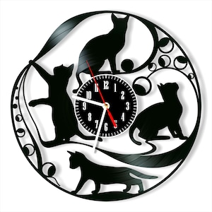 May include: Black vinyl record clock with a white clock face and black silhouette images of cats playing with a string. The clock face has black numbers and hands.