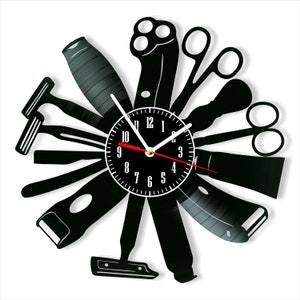 Könnte beinhalten: Eine schwarze Schallplattenuhr mit weißem Zifferblatt und schwarzen Zeigern. Die Uhr ist in Form von Friseurwerkzeugen gestaltet, darunter Rasierer, Scheren und ein Kamm.