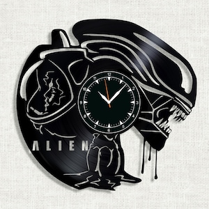 May include: Black vinyl record clock featuring a silhouette of the Alien creature from the movie franchise. The clock face is black with white numbers and hands. The text "ALIEN" is visible on the record.