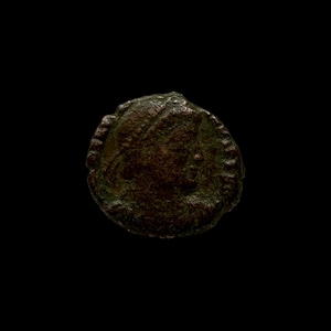May include: A close-up of a copper-colored coin with a raised design. The coin has a circular shape and a rough texture.