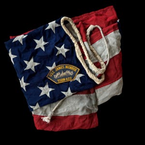May include: Vintage American flag with red and white stripes and a blue field with white stars. A patch with the text "USS JAMES MONROE SSBN-622" is sewn on the flag. A rope is draped across the flag.