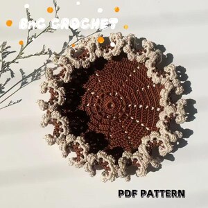 May include: A brown crochet coaster with a white crochet border. The coaster is round and has a delicate, lacy design. The text "PDF PATTERN" is visible at the bottom of the image.