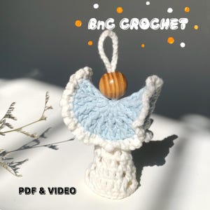 May include: A handmade crochet angel ornament with a light blue and white color scheme. The angel has a wooden bead head and a loop for hanging. The text "BnC CROCHET" is at the top, and "PDF & VIDEO" is at the bottom.