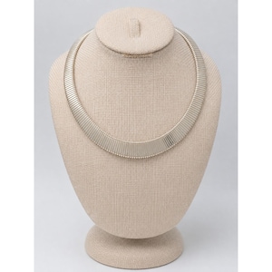May include: A gold-toned omega chain necklace featuring a wide, flat, and flexible design with a smooth, polished finish. The necklace is constructed from a series of tightly linked, horizontal segments that create a continuous, sleek, and uniform appearance.