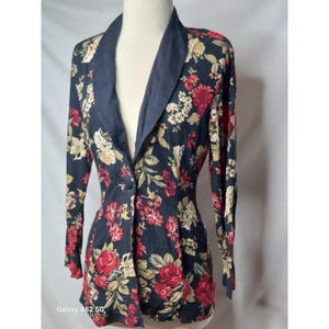 May include: A long-sleeved blazer featuring a dark navy blue base with a vibrant floral pattern in shades of red, cream, and muted green. The garment includes a solid navy blue shawl collar, a single front button closure, and a tailored fit.