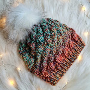 May include: A colorful knitted hat with a fluffy white pom pom. The hat is made with a variety of shades of blue, green, orange, and red yarn.