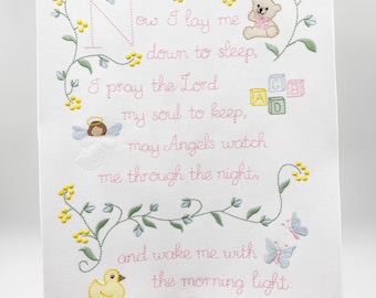 May include: Embroidered artwork featuring the prayer "Now I lay me down to sleep." The design includes a teddy bear, angel, ABC blocks, a duck, and butterflies. The text and illustrations are in pink, green, and yellow on a white background.