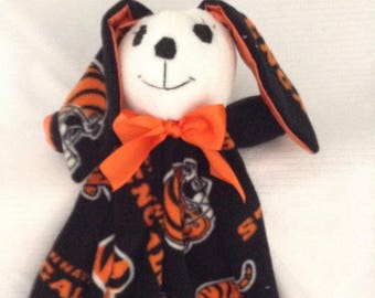 May include: A black and orange fleece baby blanket with a white bunny head attached. The blanket has a repeating pattern of orange tigers and the words "Cincinnati Bengals". The bunny has a black nose and eyes and a bright orange bow.