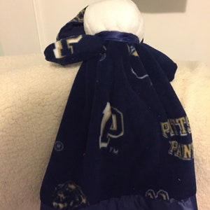 May include: A blue fleece baby blanket with a white head and a satin trim. The blanket has the Pittsburgh Panthers logo and the letters "PITT" and "PANTHERS" printed on it.