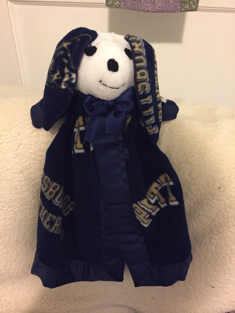 May include: A white plush bunny with a blue bow tie, wearing a blue fleece blanket with the words "Pittsburgh Panthers" in gold lettering.