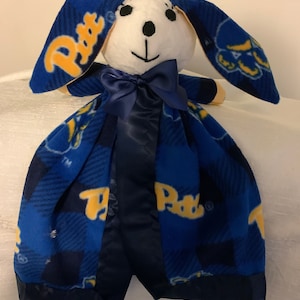 May include: A blue and yellow fleece baby blanket with a plush white bunny head attached. The bunny has black eyes and a black nose. The blanket has a blue and yellow plaid pattern with the word "Paws" repeated throughout.