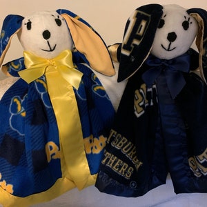 May include: Two plush bunny security blankets with a blue and gold plaid pattern. One blanket has a yellow ribbon and the other has a blue ribbon. Both blankets have the Pitt logo and the words "Pittsburgh Panthers" on them.