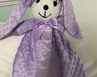 May include: A purple and white plush bunny security blanket with a satin bow. The blanket is soft and cuddly, perfect for a baby or toddler.