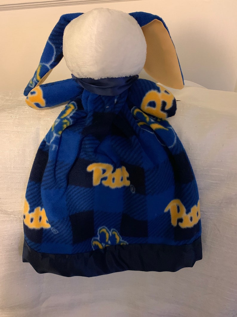 May include: Blue and yellow fleece baby blanket with a bunny head attached. The blanket has a plaid pattern with the word "Pitt" repeated on it.