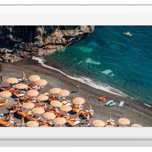 May include: An aerial view of a black sand beach with orange and white striped beach umbrellas. The beach is lined with deckchairs and there are people swimming in the clear blue water.