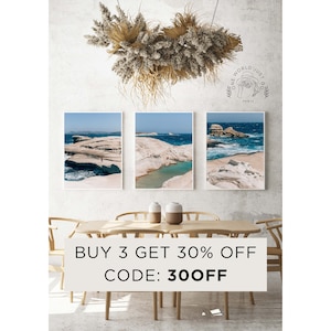 May include: Three framed photographs of a rocky coastline with turquoise water. The photos are hanging on a white wall above a wooden table with two chairs. The text "BUY 3 GET 30% OFF CODE: 30OFF" is displayed below the photos.