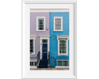 May include: A pair of colorful townhouses with a purple and blue facade. The front door is a dark blue and the windows are white. There is a black iron fence in front of the houses.